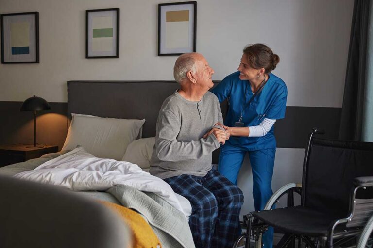 A caregiver assists an older adult in organizing daily pill containers on a well-lit kitchen table.